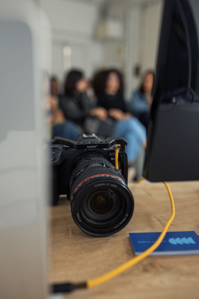Close-up of a DSLR camera on a desk in a modern office setting with people in the background.