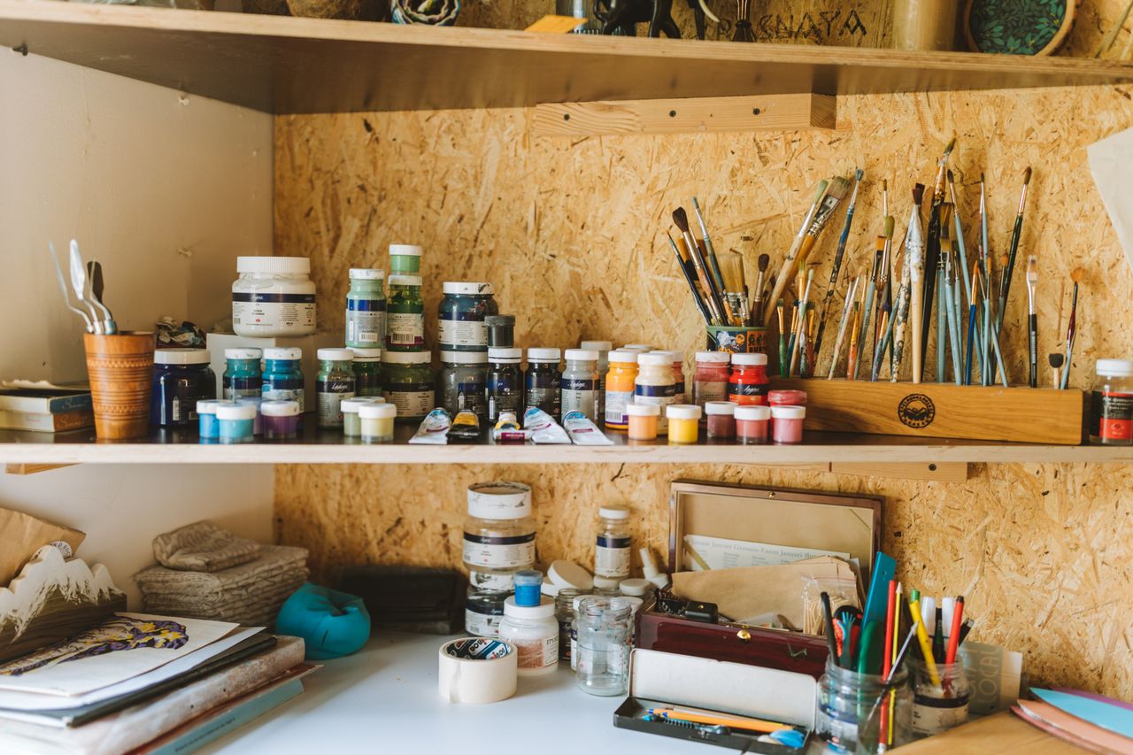 A vibrant artist's workspace filled with paints, brushes, and crafting tools on wooden shelves.